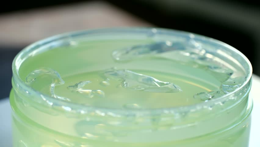 Transparent green aloe vera gel in an open jar, showcasing its smooth and cooling texture. Natural cosmetic product for skin and hair care, moisturizing, healing, and beauty treatment