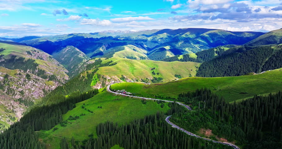 Aerial view of a winding asphalt road through lush green forests and scenic alpine hills in Xinjiang, China.