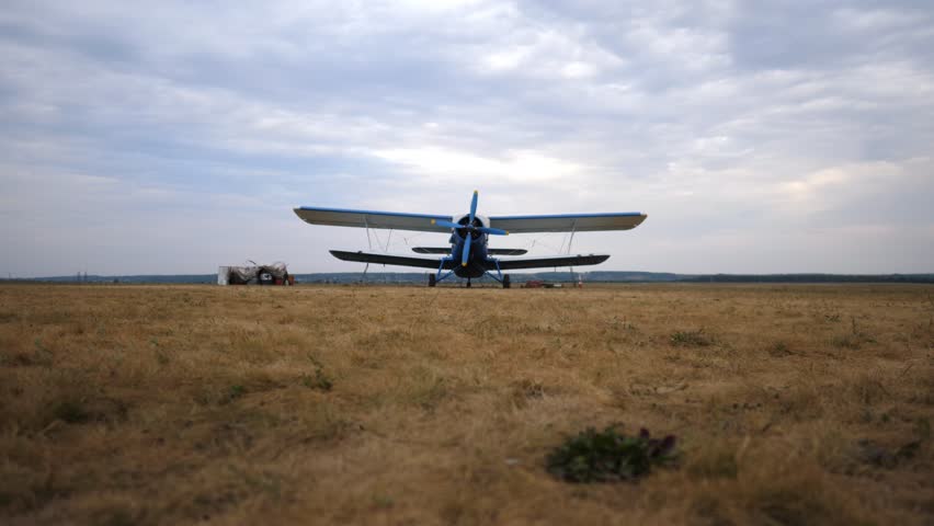 Pilot confidently approaches a parked blue aircraft on a grassy airstrip, showcasing a dynamic motion sequence of preparation and anticipation for flight in a serene outdoor setting