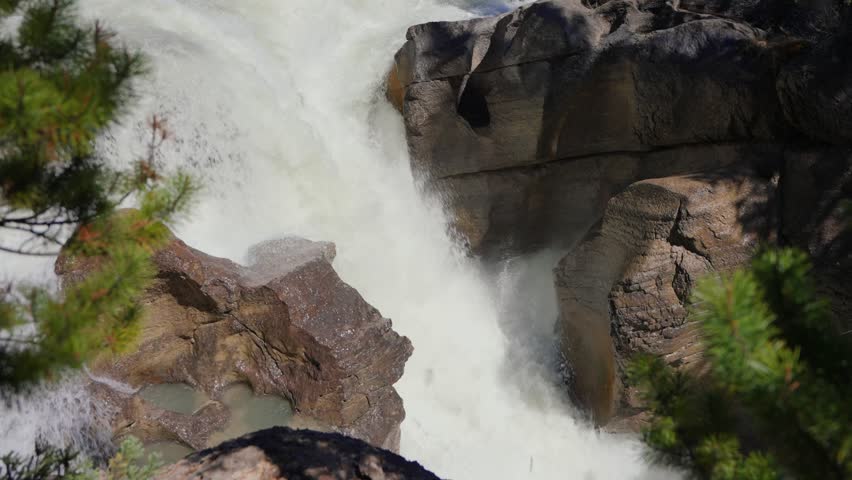 Sunwapta Falls showing powerful water flowing through a rocky canyon with mountains and forest in Jasper national park, Canada