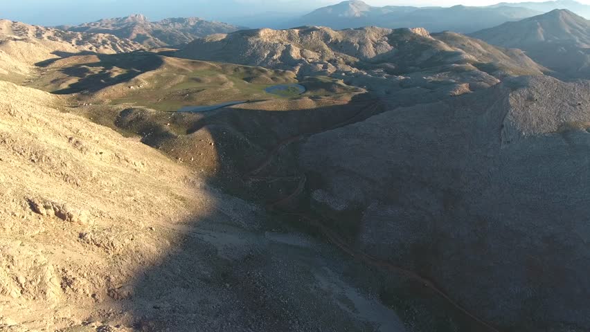 Aerial view of the Peruvian mountain ranges under sunny skies in summer. Treeless slopes, rocky valleys, and high peaks reveal the natural geography and vast terrain of the Andes. Layered relief, exposed strata, broken slopes, distant ridgelines give strong geographic structure across the entire view. Rock, soil, scrub, forest cover, open meadow patterns emphasize landform contrast shaped by climate, long erosion. Elevation change becomes especially clear where valleys, plateaus, cliffs, basins, high ridges organize visual rhythm across frame. Regional character feels convincing thanks to genuine topography, broad horizons, unforced relationships between surface texture, contour. Wide framing preserves spatial clarity, while motion direction keeps depth readable from foreground texture toward distant forms. Steady observation supports documentary realism, because composition stays clean, legible, easy to interpret during continuous movement. Panoramic sweep or fixed perspective provides usable establishing material for travel, geography, environment, atmospheric storytelling. Scale relationships remain strong, since vantage, horizon placement, gradual transitions reveal authentic proportions across terrain. Foreground detail anchors scale, middle distance builds depth, remote horizon completes convincing spatial continuity. Natural color variation separates primary forms, secondary textures, background layers without artificial stylization. Ambient mood remains consistent, giving footage polished yet realistic observational character. Visual hierarchy stays coherent, allowing eye movement across major subjects, supporting details, distant context. Lighting preserves tonal nuance, edge definition, material contrast instead of exaggerated treatment. Textural richness rewards slow viewing, because surfaces, silhouettes, motion cues remain easy to study. Additional visible cues suggest peruvian, andes, mountain, peru, aerial, peruvian andes.