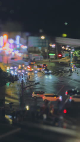 Crowds cross a rain-soaked intersection near Shilin Night Market at night, captured with a tilt-shift lens and bokeh street lights.
