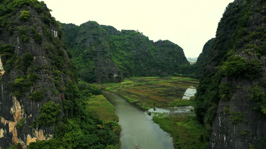 Stunning aerial perspective flying through a lush river valley surrounded by dramatic limestone karst mountains and rice paddies in Vietnam