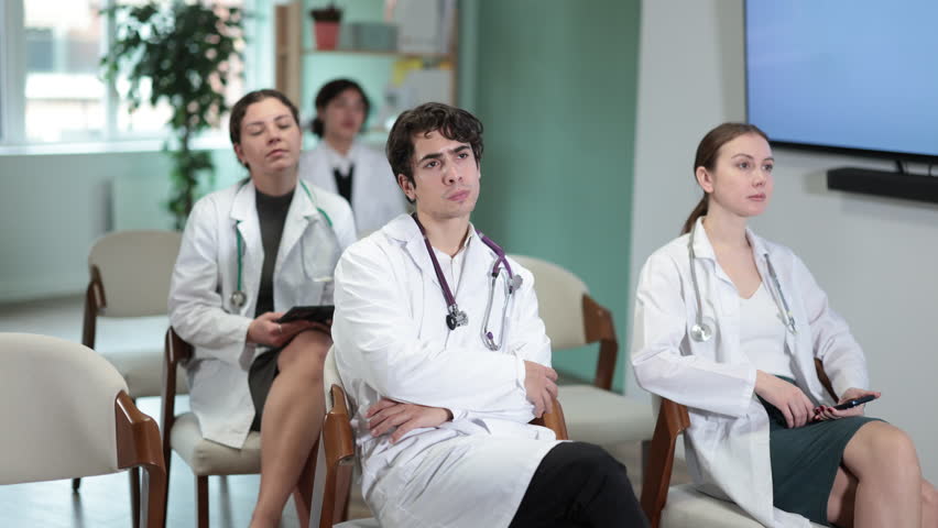 Focused group of medicals students sitting on chairs and listening lecture, taking notes on tablet in light lecture hall