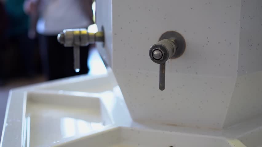 Close-up of a white marble mineral water dispenser with metal taps in a professional spa pump room.