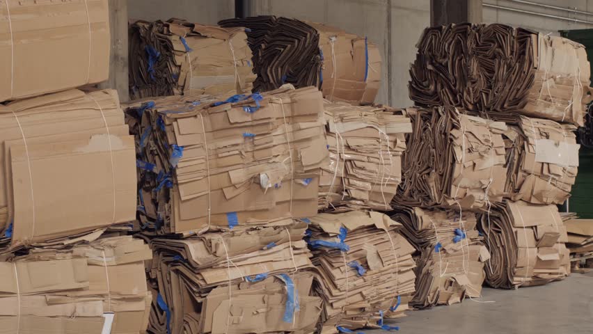 Bales of compressed cardboard are stacked in a recycling facility waiting for processing