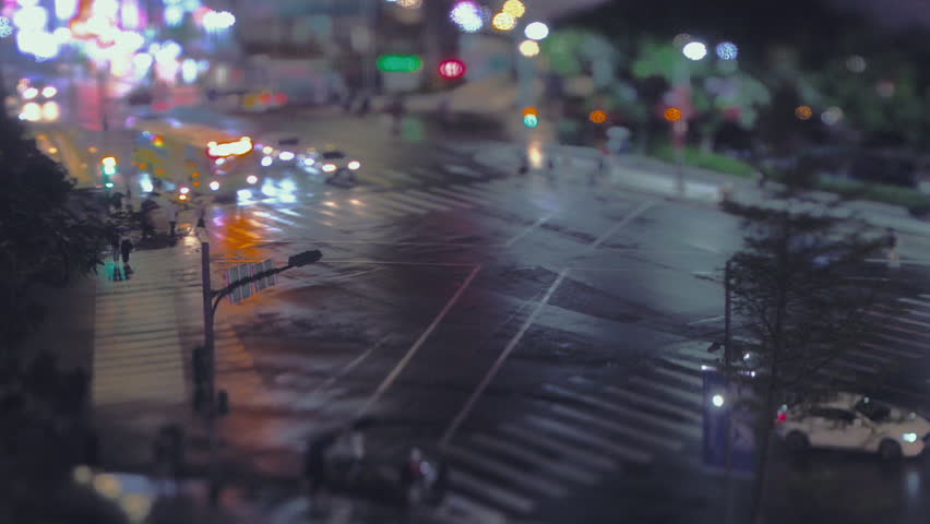 Pedestrians with umbrellas cross a busy Shilin Night Market zebra crossing at night under tilt-shift blur and neon reflections.