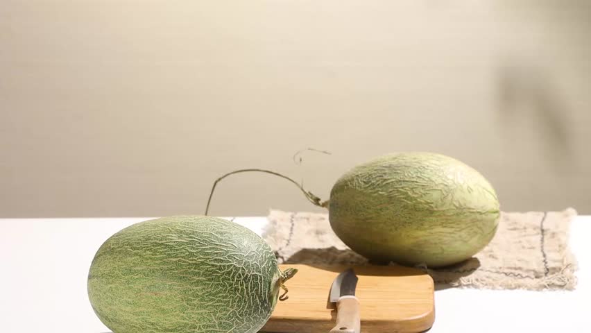 Person cutting a fresh cantaloupe melon into slices on a wooden cutting board in a kitchen