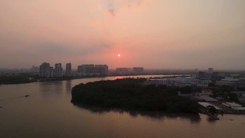 Sunrise over Saigon River and shipping port from aerial view. Camera pans to reveal view along river with ships, port infrastructure with Phu My Bridge and urban development in the background.