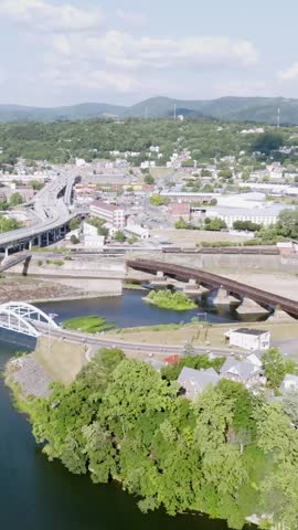 Vertical aerial drone pan right to left over Cumberland Maryland showcasing cityscape buildings and surrounding landscape in daylight