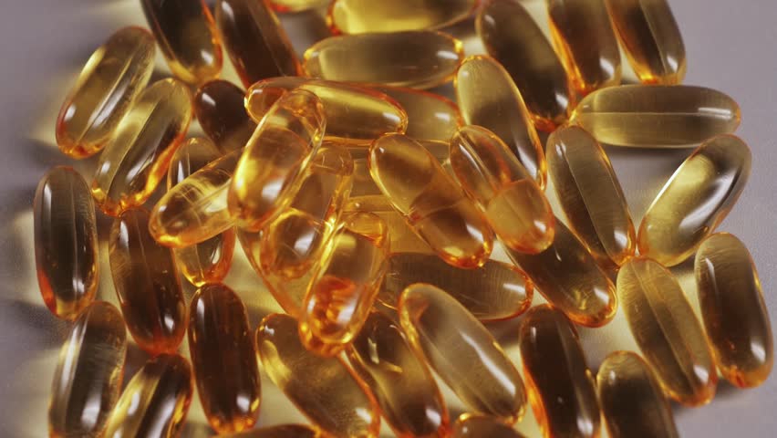 A close-up of Omega-3 capsules, clear, golden, and glossy. The soft gel capsules are filled with fish oil on a surface. Health and daily wellness support. High quality 4k footage