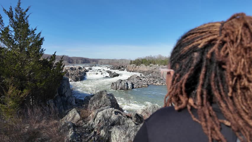 Woman looking at the rocky river rapids and waterfalls on a sunny day