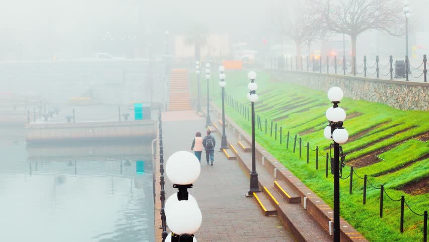 Victoria, BC, Canada – March 30, 2026: People stroll through dense morning fog at the Inner Harbour causeway