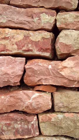 Close-up of a rustic dry-stone wall made of stacked red sandstone blocks. Natural building material background with rough texture