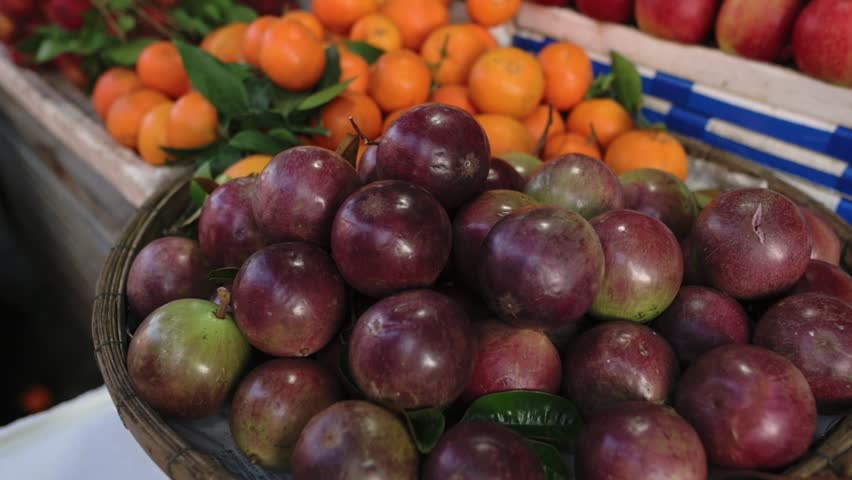 Vietnam Street Market Stall With Vendor Hand Selecting Ripe Plums In Woven Basket, Mandarin Oranges And Apples In Background, Closeup Texture, Fresh Produce Vibe And Morning Light.