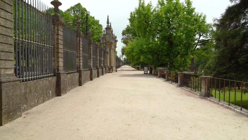 Long sandy pathway lined with ornate fence and lush green trees