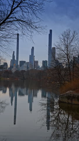 New York City skyline reflection in Central Park lake. Manhattan skyscrapers reflected in the still water of a lake surrounded by bare winter trees.