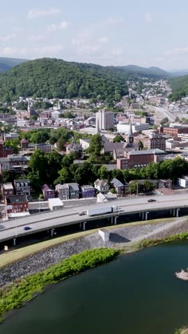 Vertical aerial drone shot moving left to right over Cumberland Maryland showcasing cityscape architecture and surrounding landscape in daylight