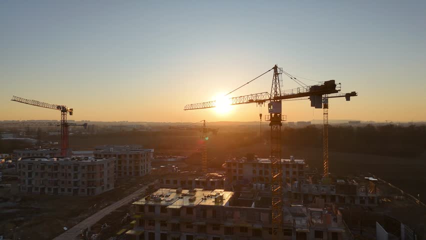 Aerial view of modern residential complex construction with cranes at sunset. Construction site at golden hour with cranes and building progress. Concept of urban development. Vibrant colors of sky