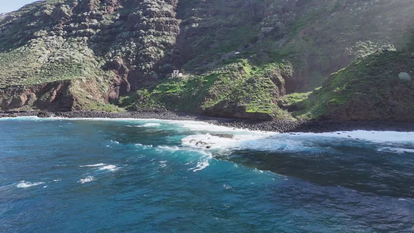 Coastal landscape featuring rocky shoreline and crashing waves, with lush green hills in the background and clear blue sky above, capturing the serene beauty of nature