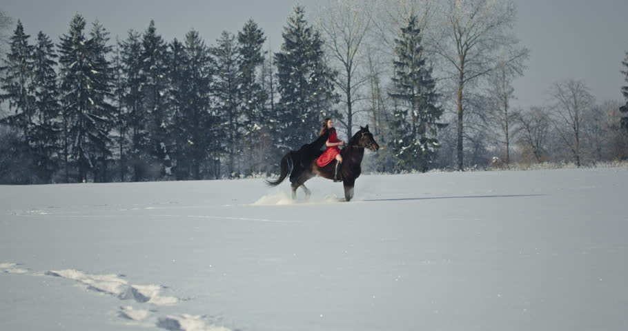 Woman in red dress galloping horse through snowy field