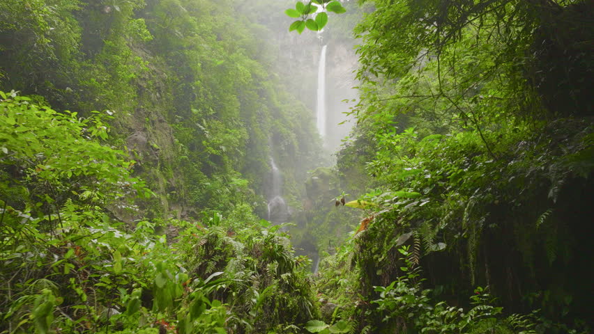 Drone view of a scenic waterfall cascading through dense rainforest in Costa Rica, surrounded by vibrant tropical greenery and dramatic jungle landscape.