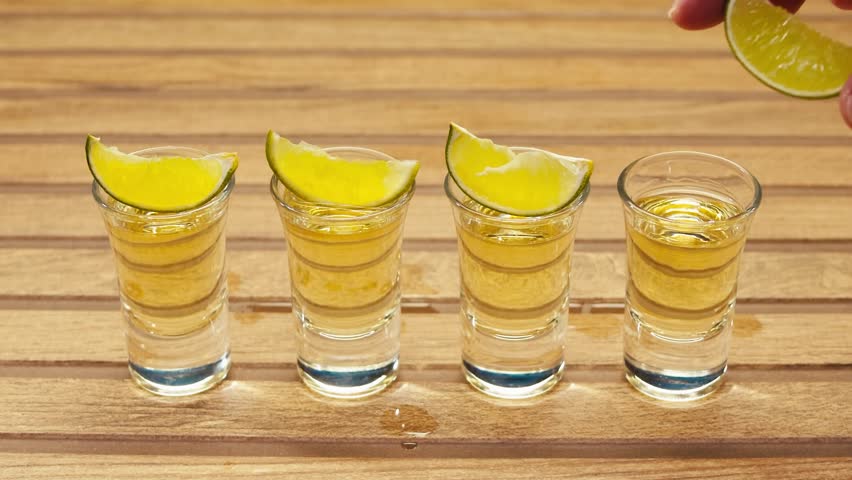 Mexican Tequila Mezcal pouring with lime and salt on a stone table. Strong vodka rum alcoholic drink is poured from a bottle into a shots.