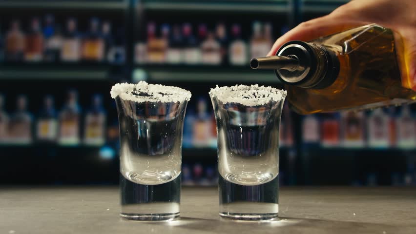 Mexican Tequila Mezcal pouring with lime and salt on a stone table. Strong vodka rum alcoholic drink is poured from a bottle into a shots.