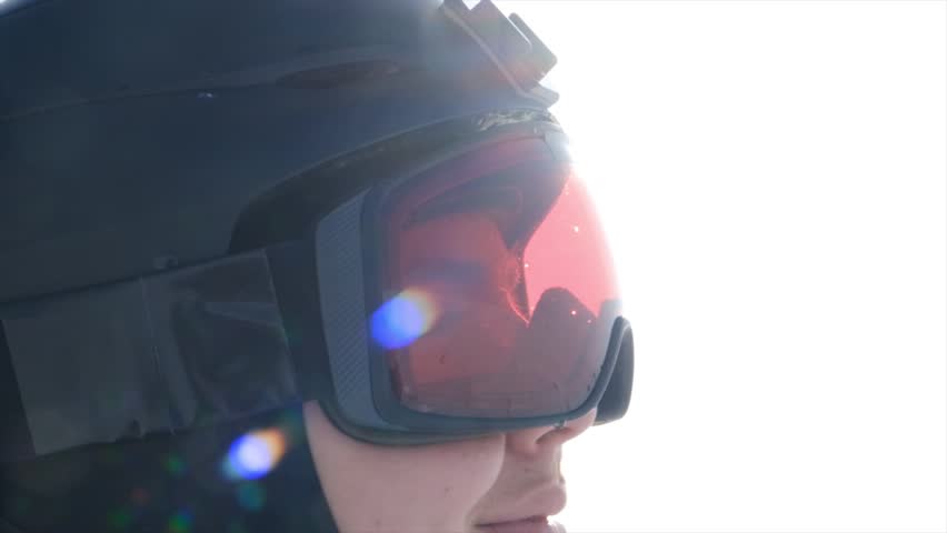 Close up head of skier in helmet and ski goggles smiling and looking forward anticipating excitement and adrenaline before descent. Happy snowboarder ready to start. Winter sport and active lifestyle