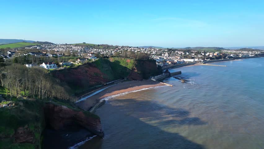 Dawlish, Devon, England: DRONE VIEWS: An intercity train passes through a cliff tunnel and emerges the other side on its way towards Dawlish railway station.
Dawlish is a popular UK tourist destination on the mainline railway to London Paddington; the town is famous for its resident population of black swans.