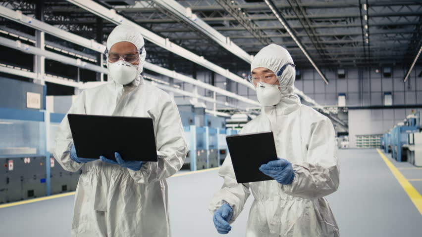 Monitoring microchip production, devices and engineering team brainstorming in factory cleanroom. Supervising semiconductors manufacturing, protective gear and teamworking colleagues, camera A