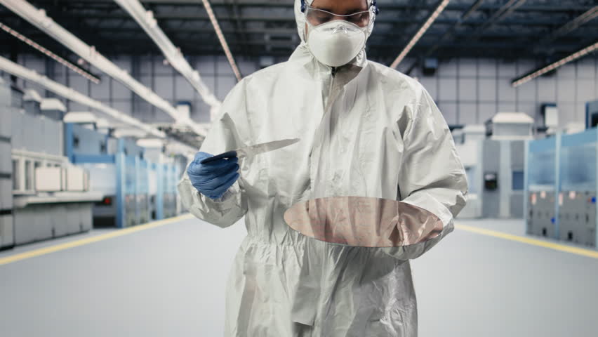 Technician examining semiconductor substrate in cleanroom of PCB manufacturing plant. Employee in safety gear verifying optical photolithography patterns on high tech silicon wafer component, camera A