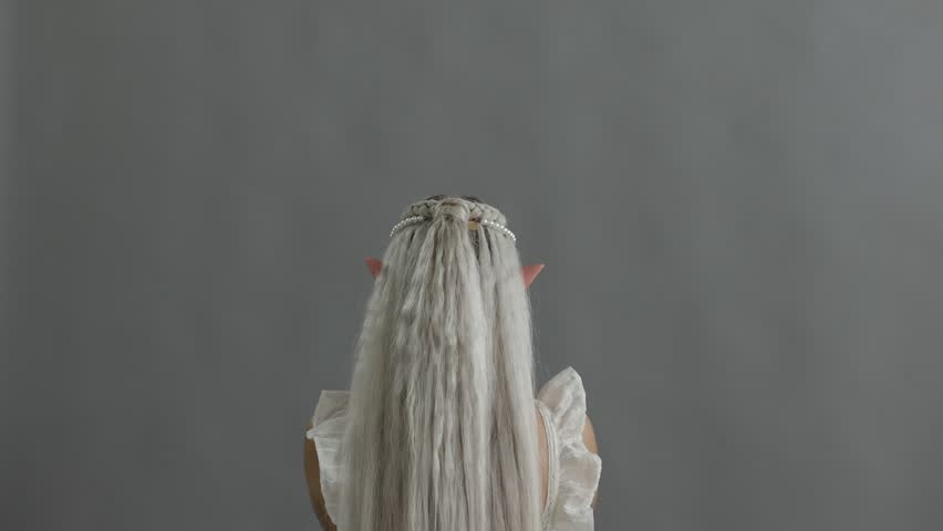 Beautiful girl dressed as elf with glass ball on grey background