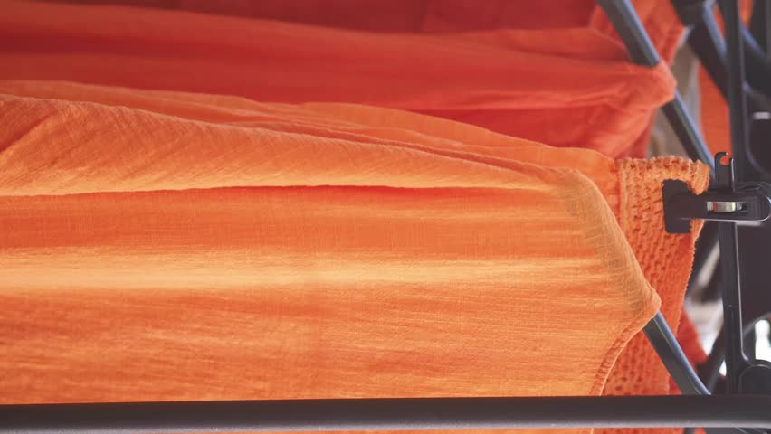 Close up of bright orange fabric folds and creases, soft textile texture and draped material on metal frame.