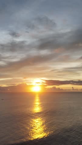 Breathtaking sunset over a calm beach with dramatic clouds and golden reflections on shallow water, featuring silhouettes of people enjoying the peaceful seaside atmosphere.