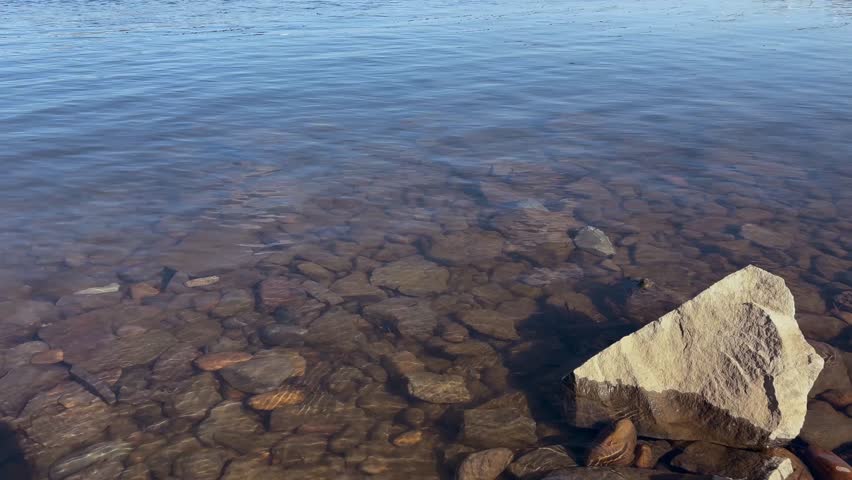 Rocky river bottom through clear water with a stone in the foreground. Clean Mountain Stream Video Footage.