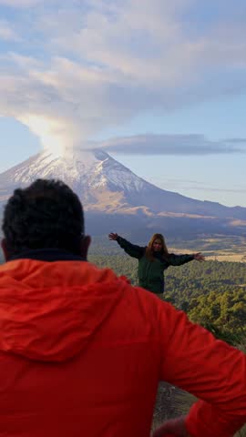 Couple reaching a viewpoint and hugging while looking at the active popocatepetl volcano