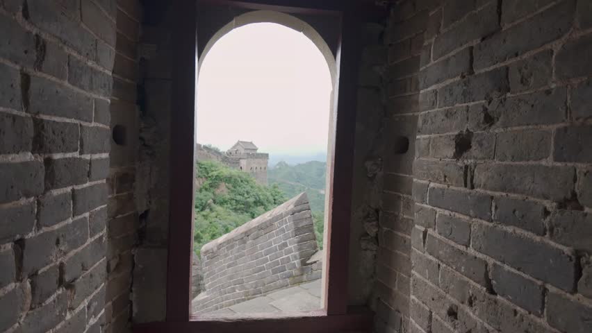 A cinematic reveal of the Great Wall of China winding across lush green mountains, seen through an ancient stone watchtower archway. Perfect for travel documentaries and historical content.