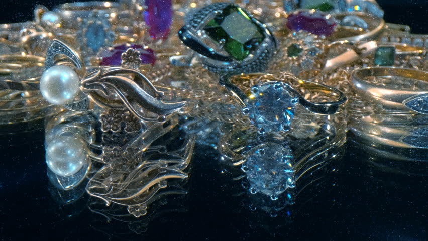 Beautiful shiny, sparkling golden jewelry on a glass surface with glare in gems.  View through sparkling particles. Macro. Closeup. Shallow depth of field. Shot in motion