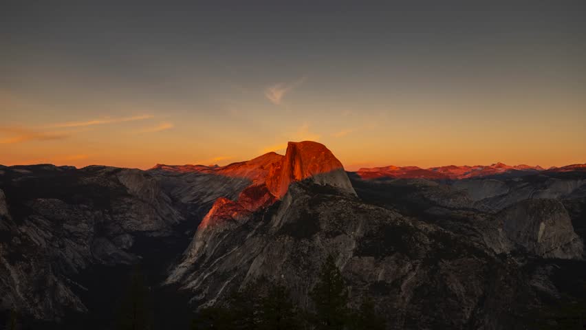 This 4K video captures Half Dome in Yosemite National Park during sunset. The visual documents the granite batholith and Yosemite Valley from the Glacier Point overlook. The composition illustrates the orange illumination on the rock face and clouds, documenting Sierra Nevada geology and high-country topography for nature, travel, and editorial media.