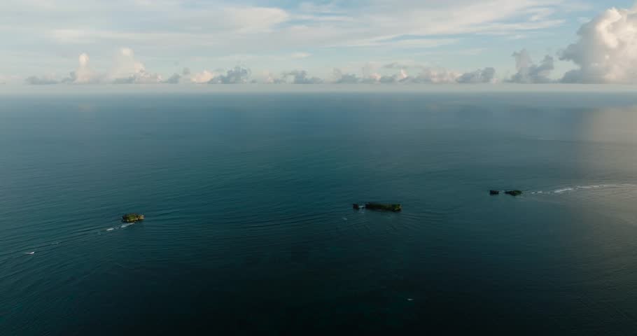 Two small rocky islands rise from the calm ocean surface. Siargao, Philippines.