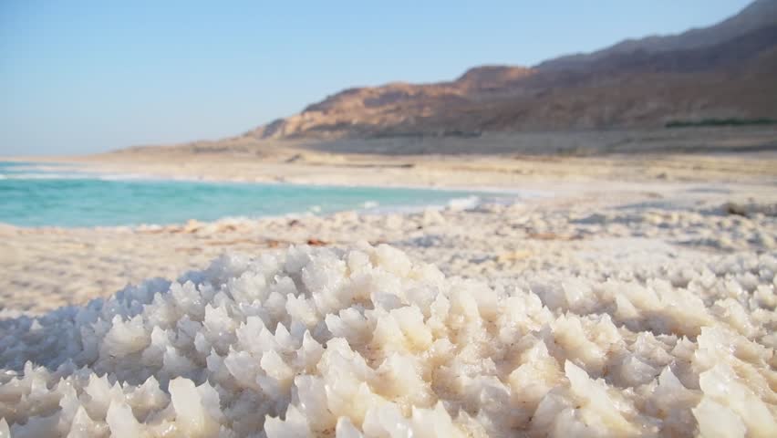 Close up Dead Sea salt crystals on shoreline beach in Jordan at sunset with turquoise water desert coast lowest point on Earth landscape. Jordan - Israel border line zone