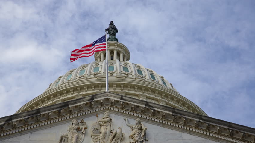American flag on historic Capitol. American flag in patriotic sky. American flag for governance symbol. American flag on iconic dome.