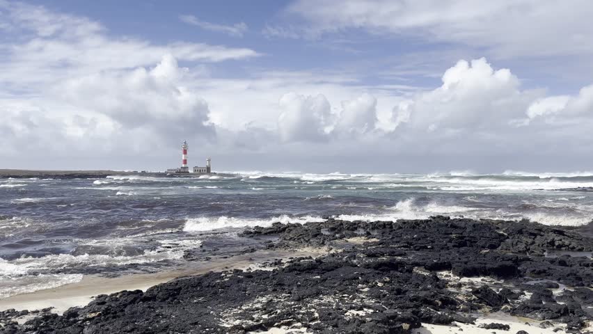 Scenic Coastal View with Distant Lighthouse, Historic lighthouse standing on a rocky shoreline with ocean waves crashing.