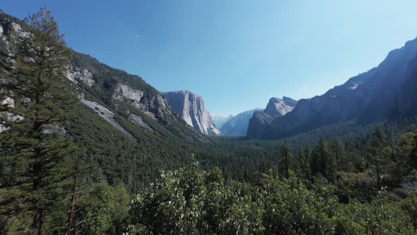 This 4K video captures the Tunnel View overlook in Yosemite National Park. The visual documents the granite face of El Capitan, Bridalveil Fall, and Half Dome in the distance. The composition illustrates the U-shaped valley carved by glaciers, documenting Sierra Nevada geomorphology and 1933 viewpoint infrastructure for nature, travel, and editorial media.