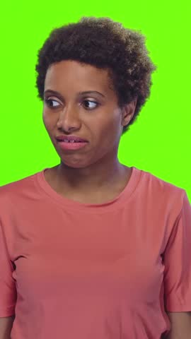 Young African American woman reacts to bad smell holding nose with disgust and surprise on green background. Emotion, reaction and unpleasant odor concept in casual clothing.