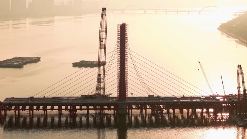 Aerial view of bridge demolition in China, cable-stayed structure being dismantled with cranes over river on the sunset