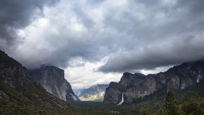This 4K video captures the Tunnel View overlook in Yosemite National Park, California. The visual documents the granite face of El Capitan and Bridalveil Fall under storm cloud cover. The composition illustrates the U-shaped valley topography and Sierra Nevada mountain weather patterns, documenting glacial geomorphology and atmospheric conditions for nature, travel, and editorial media.