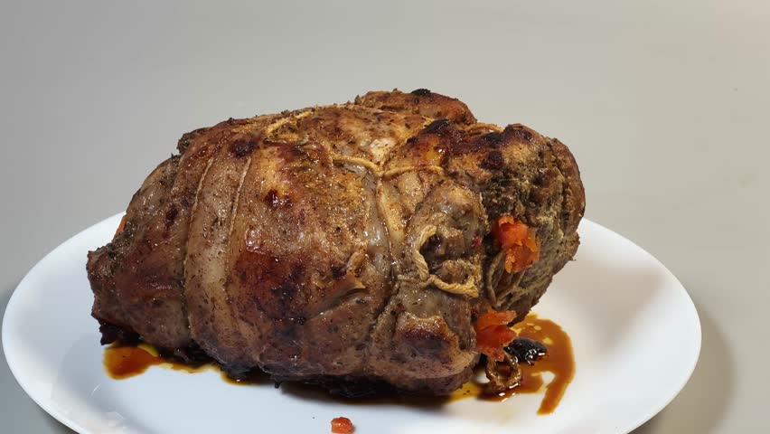 Big piece of baked pork neck with spices, stuffed with carrots and garlic and tied with cotton culinary twine on a plate on a gray background, front view while approach
