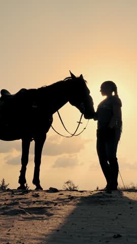 Horse riding. Horse love. Silhouettes of a young woman and her horse, at sunset, on sky background and sun rays backlight. friendship between man and horse. Equitation.